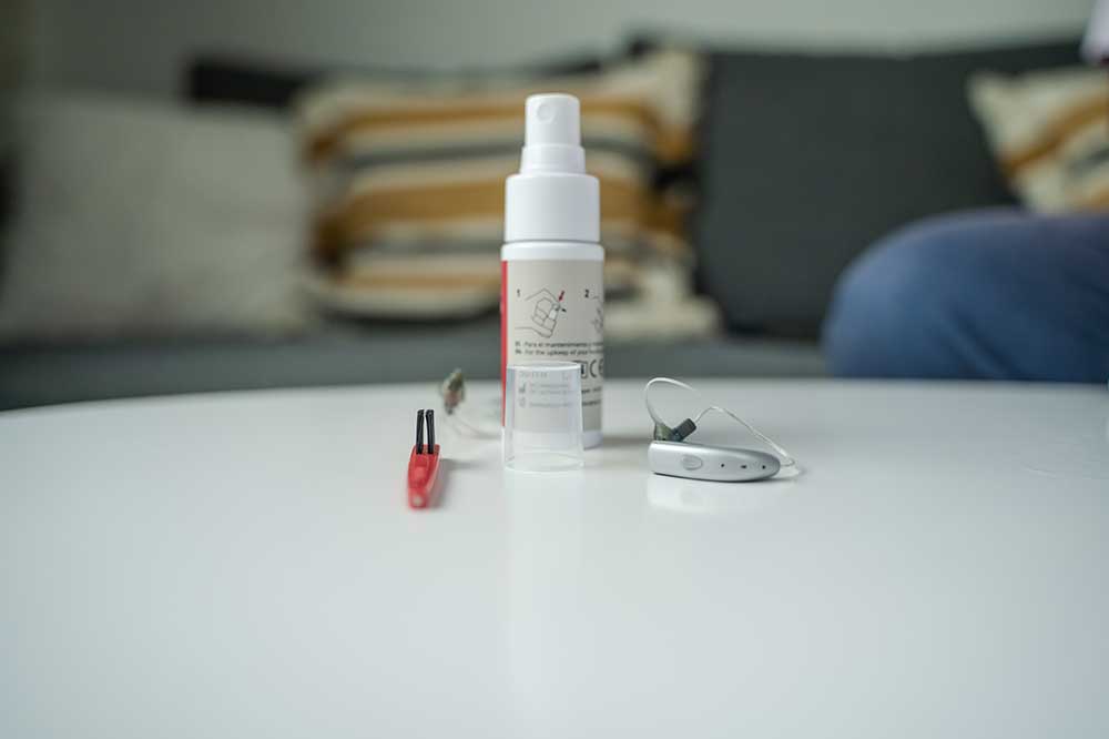 Cleaning spray, red brush and a behind-the-ear hearing aid on a table, hearing aid care tools at New River Valley Hearing & Balance in Radford, VA