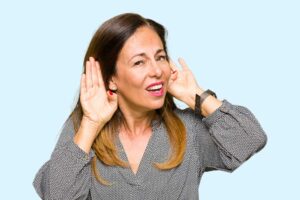 Woman cupping both hands behind her ears to hear better, as when hearing aids sound uneven, at New River Valley Hearing & Balance in Radford, VA